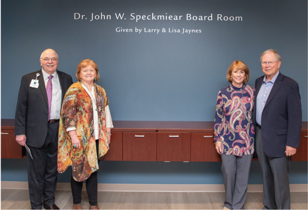 Four people smiling in front of a wall that reads Dr. John W. Specter Board Room